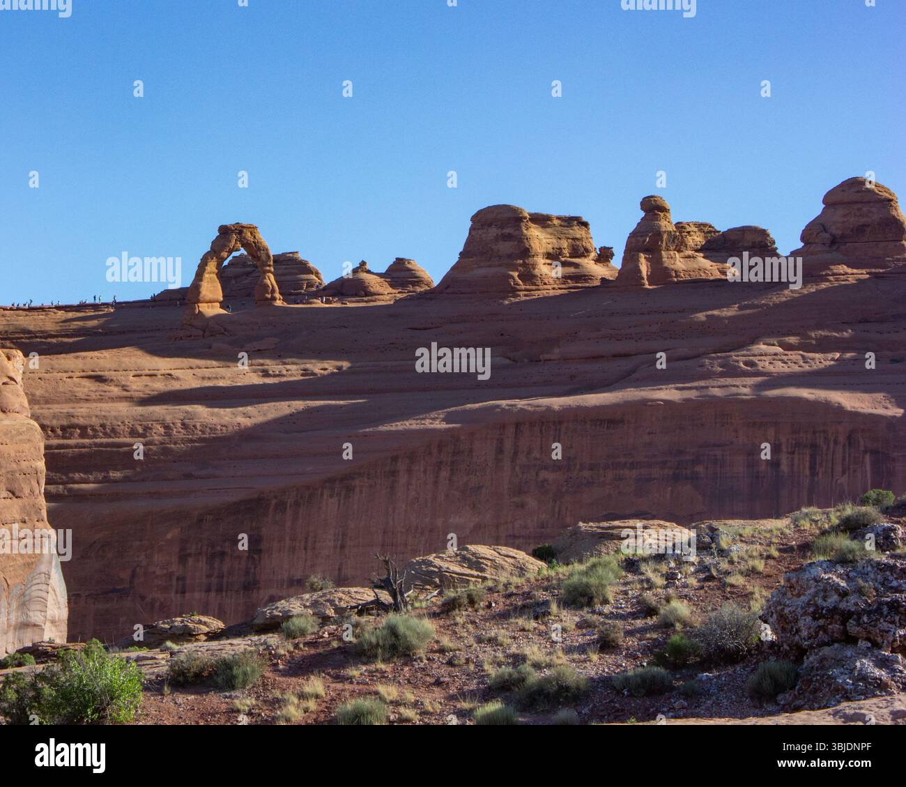 Des formations rocheuses uniques s'élèvent contre un ciel bleu clair, mettant en valeur une arche naturelle entourée d'un terrain désertique aride et d'une végétation clairsemée pendant M. Banque D'Images