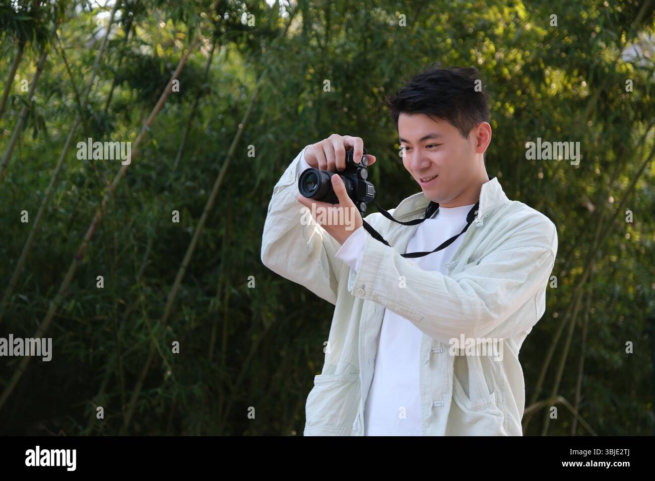 Beau jeune homme asiatique prenant des photos à l'aide d'un appareil photo numérique en plein air Banque D'Images
