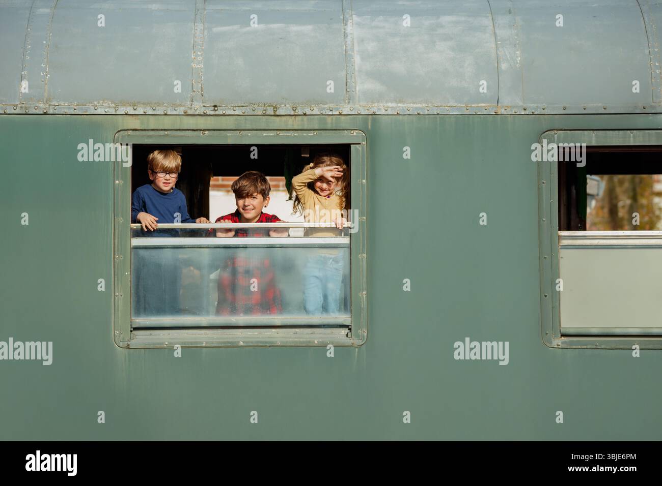 Trois enfants se penchent devant la fenêtre du train qui donne sur la campagne Banque D'Images