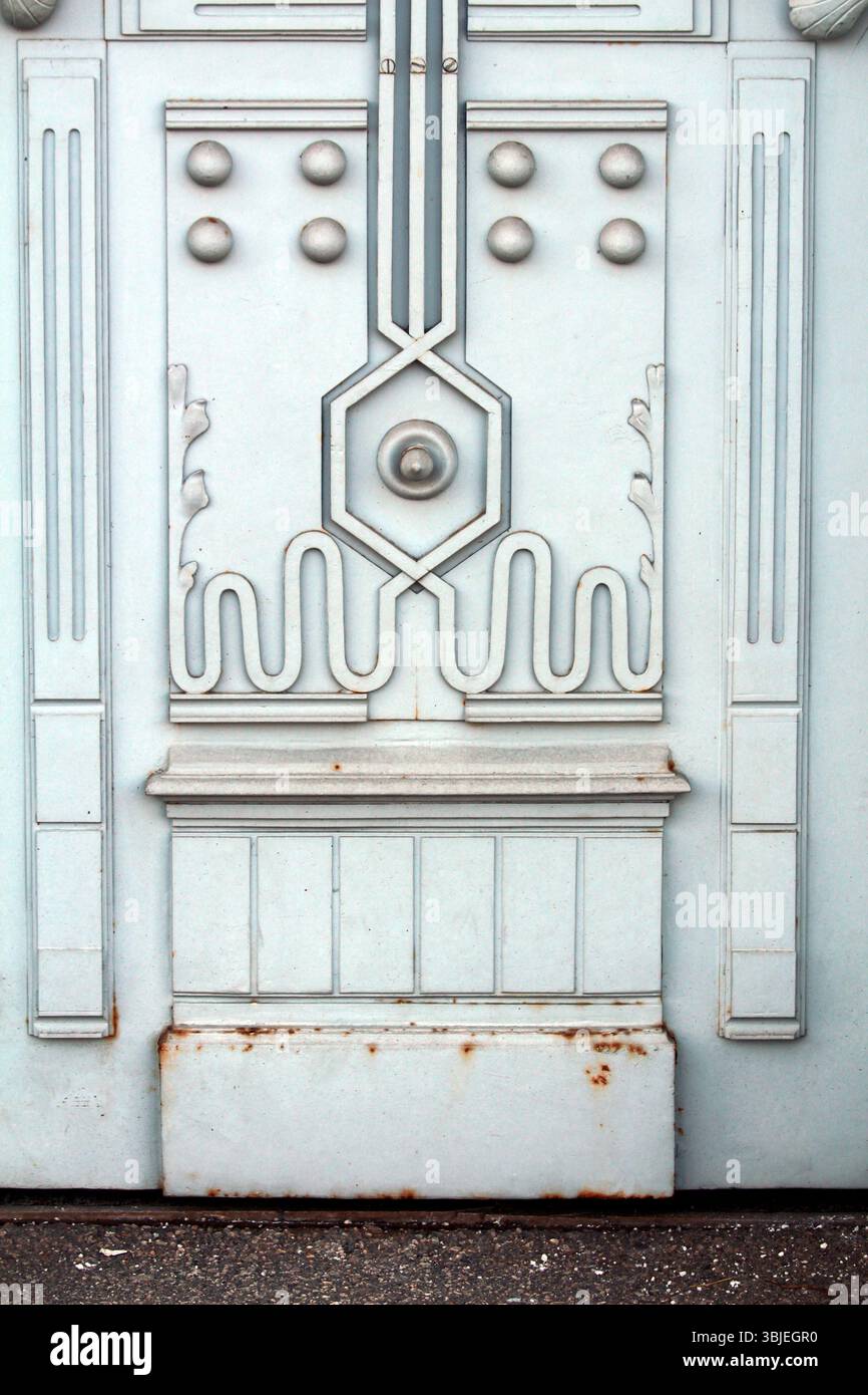 Gros plan d'une porte en métal pâle ornée aux formes géométriques, aux pois en relief et aux motifs floraux stylisés, montrant de subtiles intempéries et de la rouille près du Banque D'Images