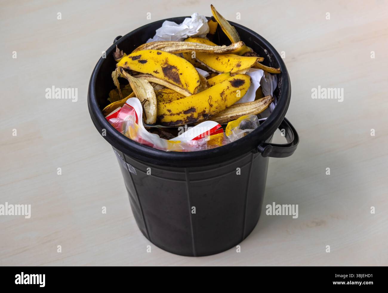 Seau en plastique noir rempli d'ordures ménagères et de déchets. Pelures de banane visibles, papier, mouchoirs, sacs en polyéthylène. Banque D'Images
