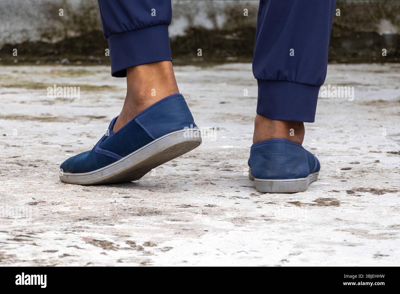 Pied masculin avec baskets bleu marine sur béton. Chaussures pour hommes élégantes, à la mode et confortables, vue arrière en gros plan. Banque D'Images