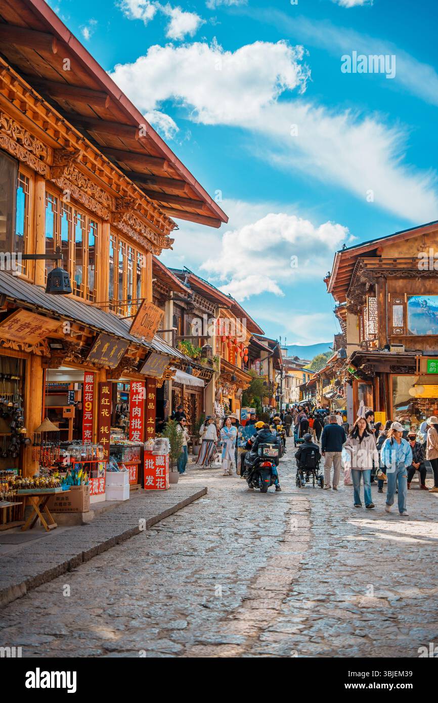Shangri-la, Chine - 20 octobre 2024 : une rue animée dans l'ancienne ville de Dukezong bordée de bâtiments traditionnels en bois et de boutiques sous un ciel lumineux. Banque D'Images