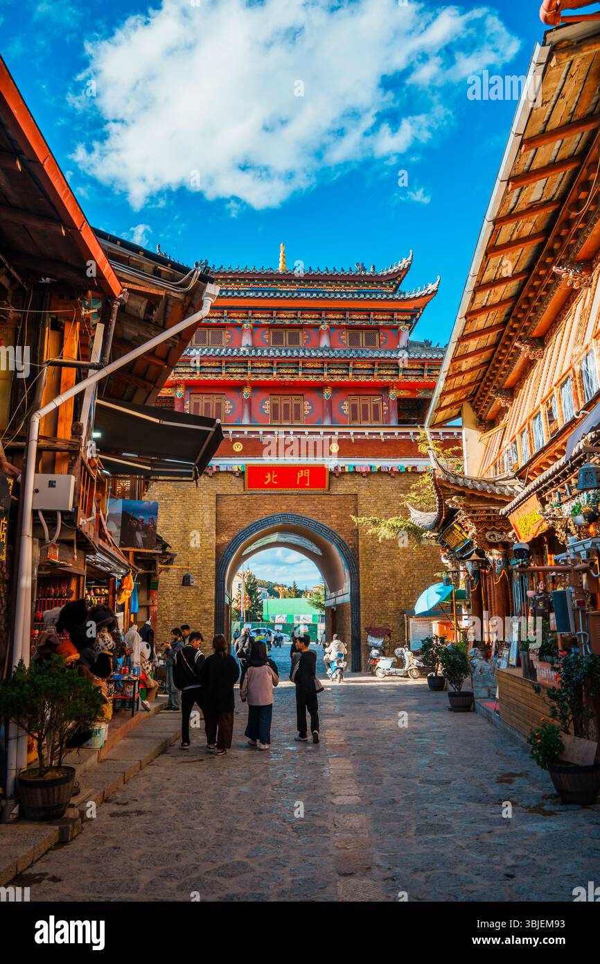 Shangri-la, Chine - 20 octobre 2024 : les touristes traversent l'arche traditionnelle de la ville antique de Dukezong sous un ciel bleu clair. Banque D'Images