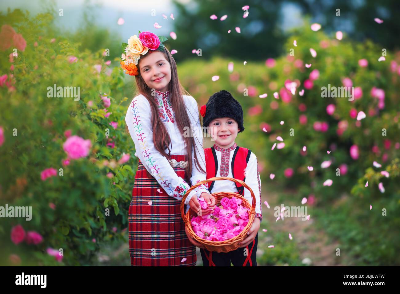 Vallée des roses bulgares près de Kazanlak, Bulgarie et fille et garçon frères et sœurs dans des vêtements de folklore ethnique récoltant des roses oléagineuses florissantes au lever du soleil Banque D'Images