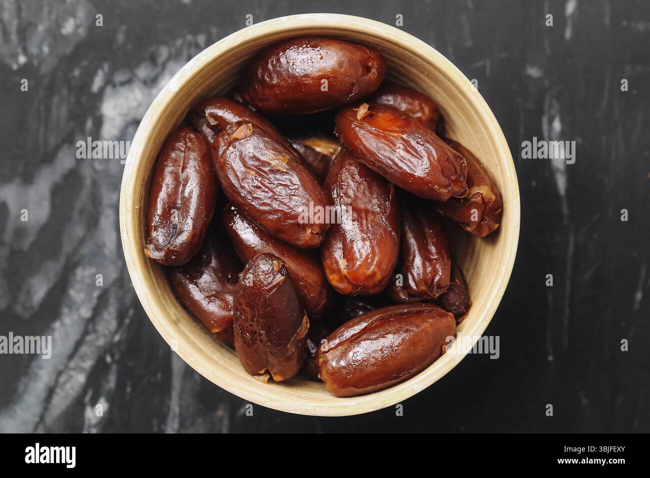 Dattes séchées dans un bol. Faire revenir les fruits sucrés. Collation saine biologique. Aliments énergétiques naturels. Ingrédient végétalien rustique. Fond de texture de marbre. Macro gros plan. Banque D'Images