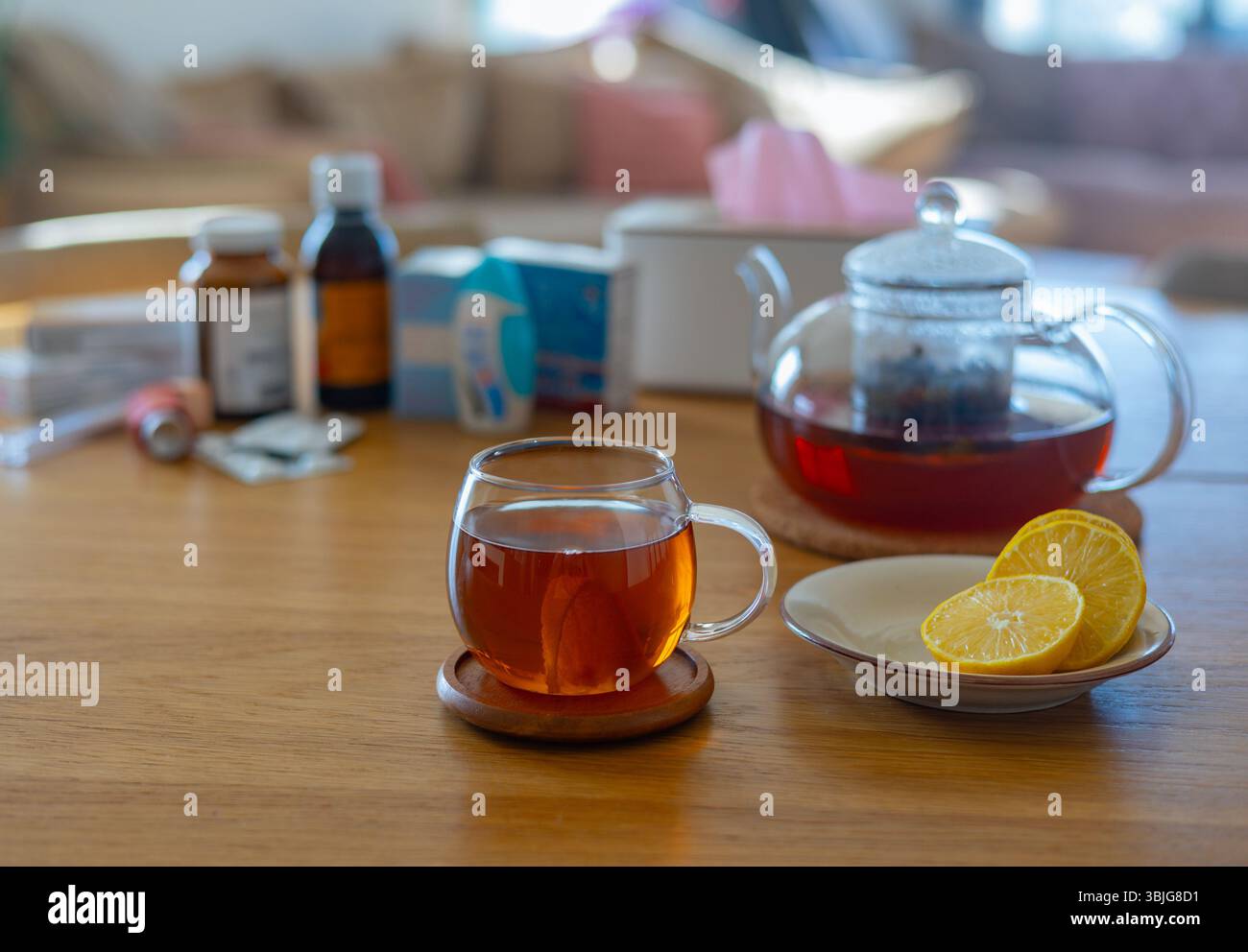 Une tasse de verre de tisane chaude avec du citron se trouve sur une table en bois près de médicaments et d'une théière Banque D'Images