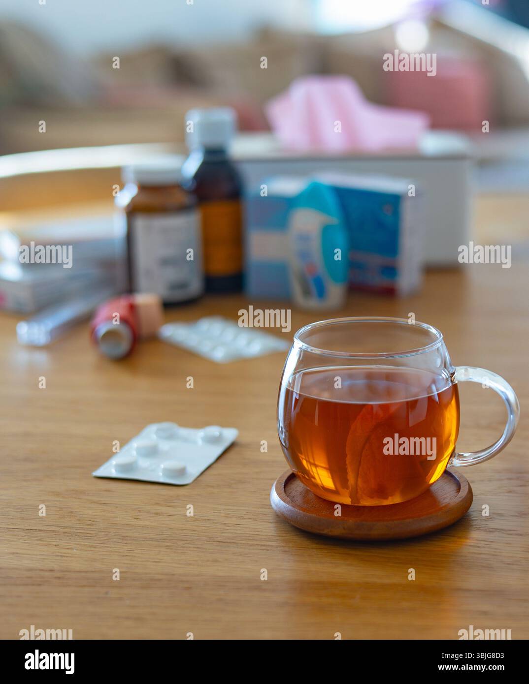 Une tasse de verre de tisane chaude avec du citron se trouve sur une table en bois près de médicaments et d'une théière Banque D'Images