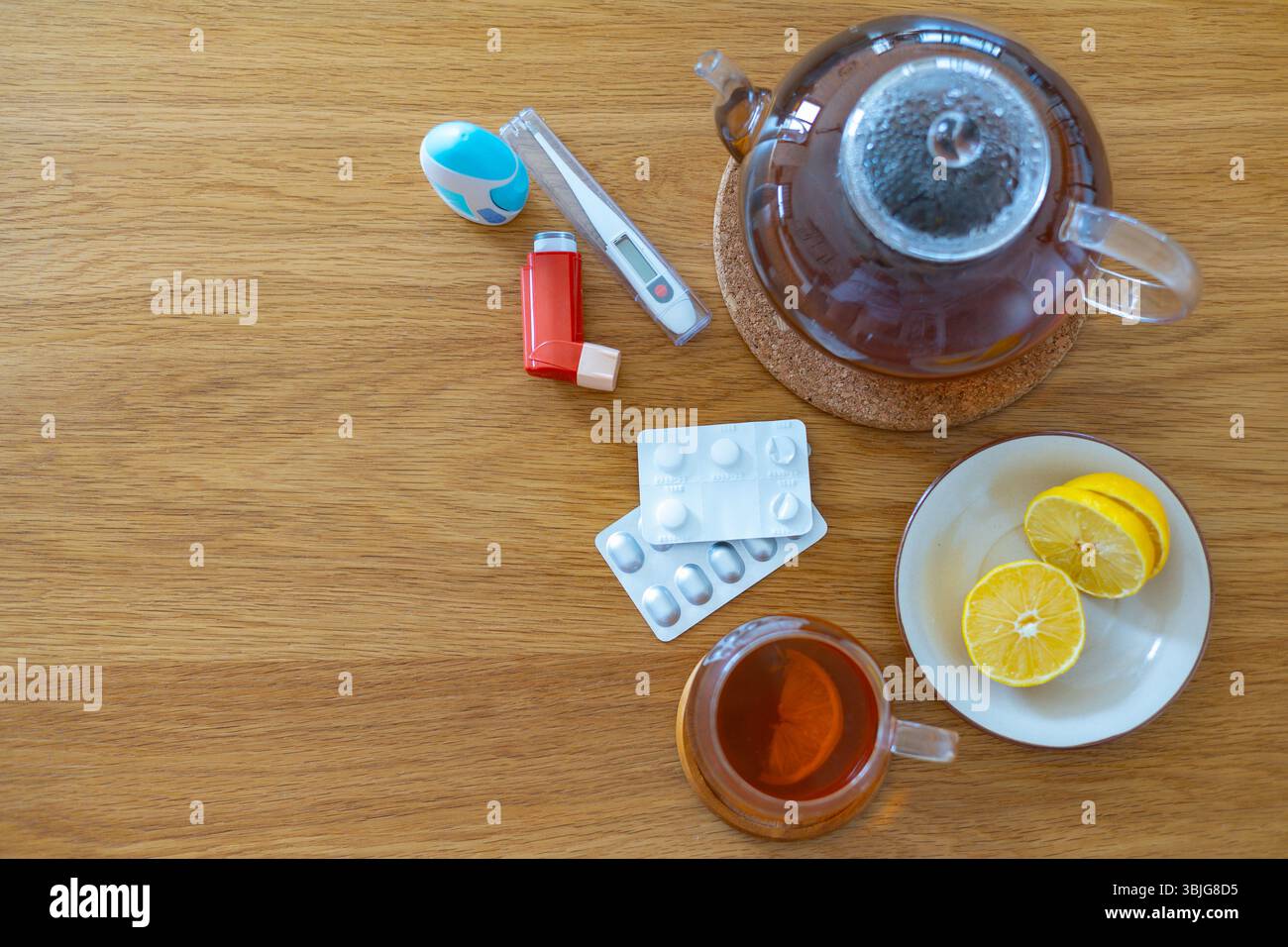 Flatlay de soins à domicile essentiels pour le rhume ou la grippe : une tasse et une théière avec du thé, du citron tranché sur une assiette, inhalateur, thermomètre, blister de médicament Banque D'Images