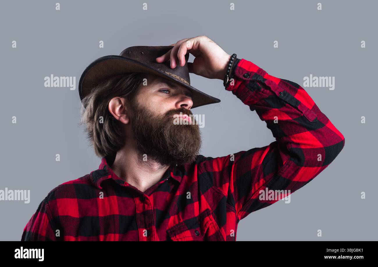 Chapeau de cow-boy. Homme barbu en chemise à carreaux et chapeau de cow-boy. Cow-boys en chapeau en cuir et chemise à carreaux. Portrait d'un jeune beau macho barbu en cow-boy Banque D'Images