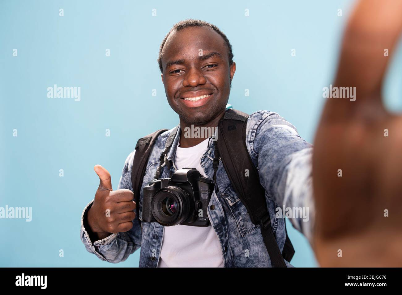 Vlogger masculin afro-américain donnant les pouces à son public en ligne, s'enregistrant lui-même en studio. POV de photographe noir joyeux faisant un geste d'accord vers l'appareil photo. Banque D'Images