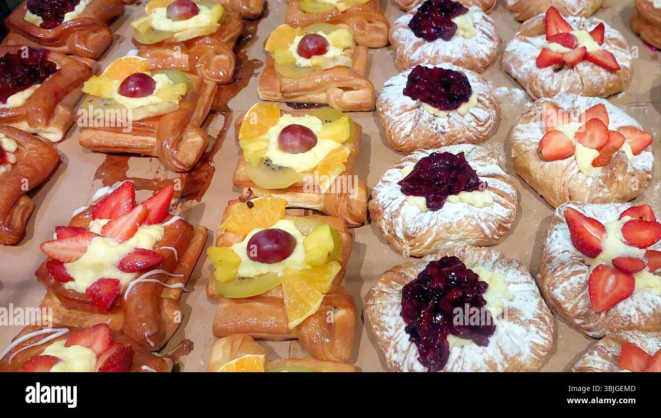 Des rangées de pâtisseries sucrées assorties présentent des fruits vibrants et des garnitures crémeuses, invitant les clients à se livrer à ces délicieuses friandises dans une boulangerie locale Banque D'Images