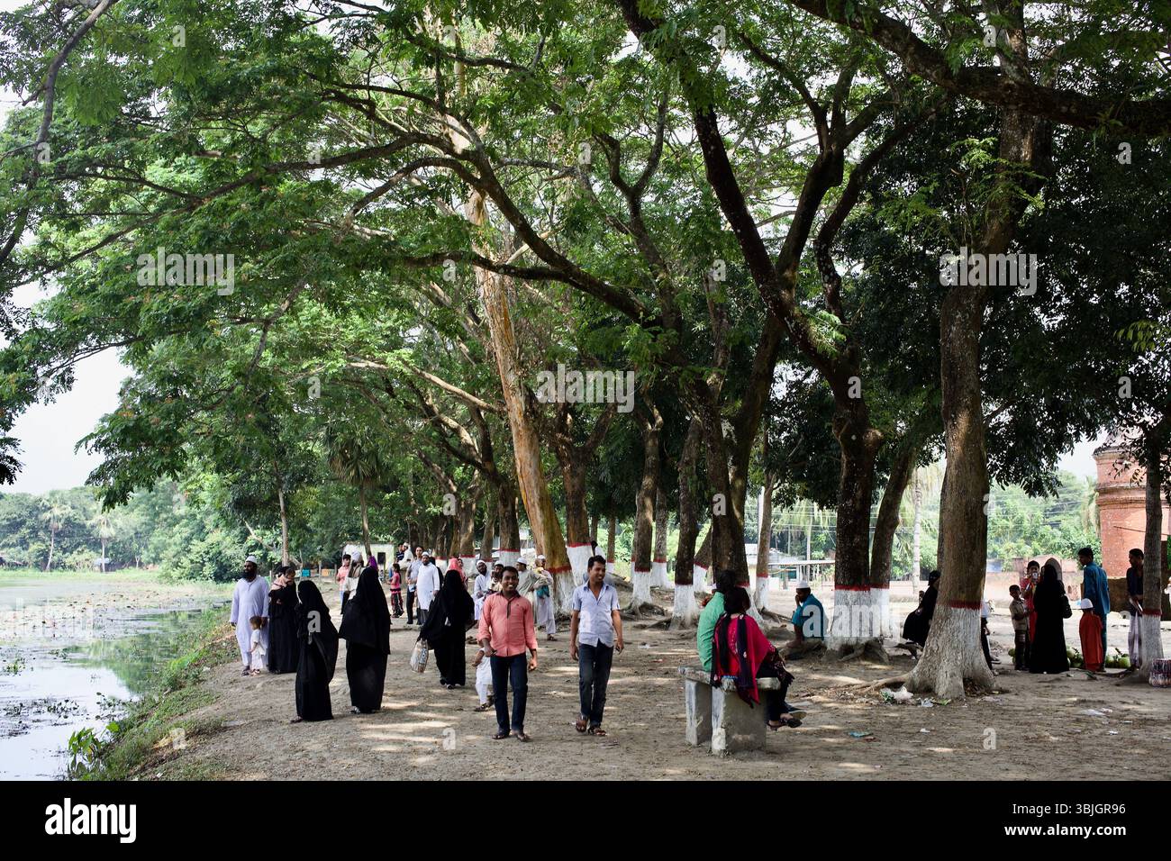 Les visiteurs se promènent sous les arbres le long de l'étang de Ghora Dighi près de la Mosquée historique Sixty Dome à Bagerhat, au Bangladesh. Banque D'Images