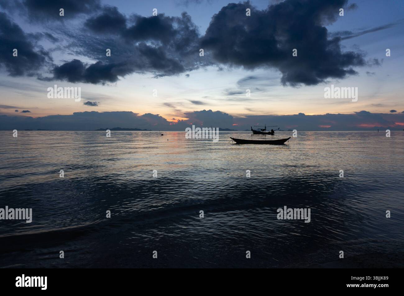 Crépuscule sur une mer tranquille avec des bateaux de pêche silhouettes Banque D'Images