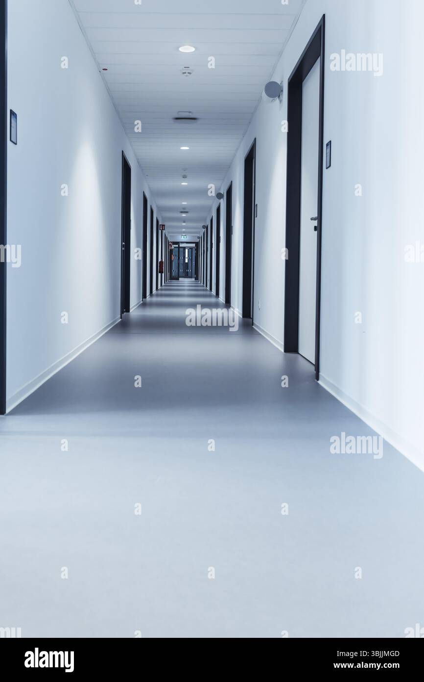 Un long couloir étroit d'une école moderne ou d'un immeuble de bureaux avec plusieurs portes fermées Banque D'Images
