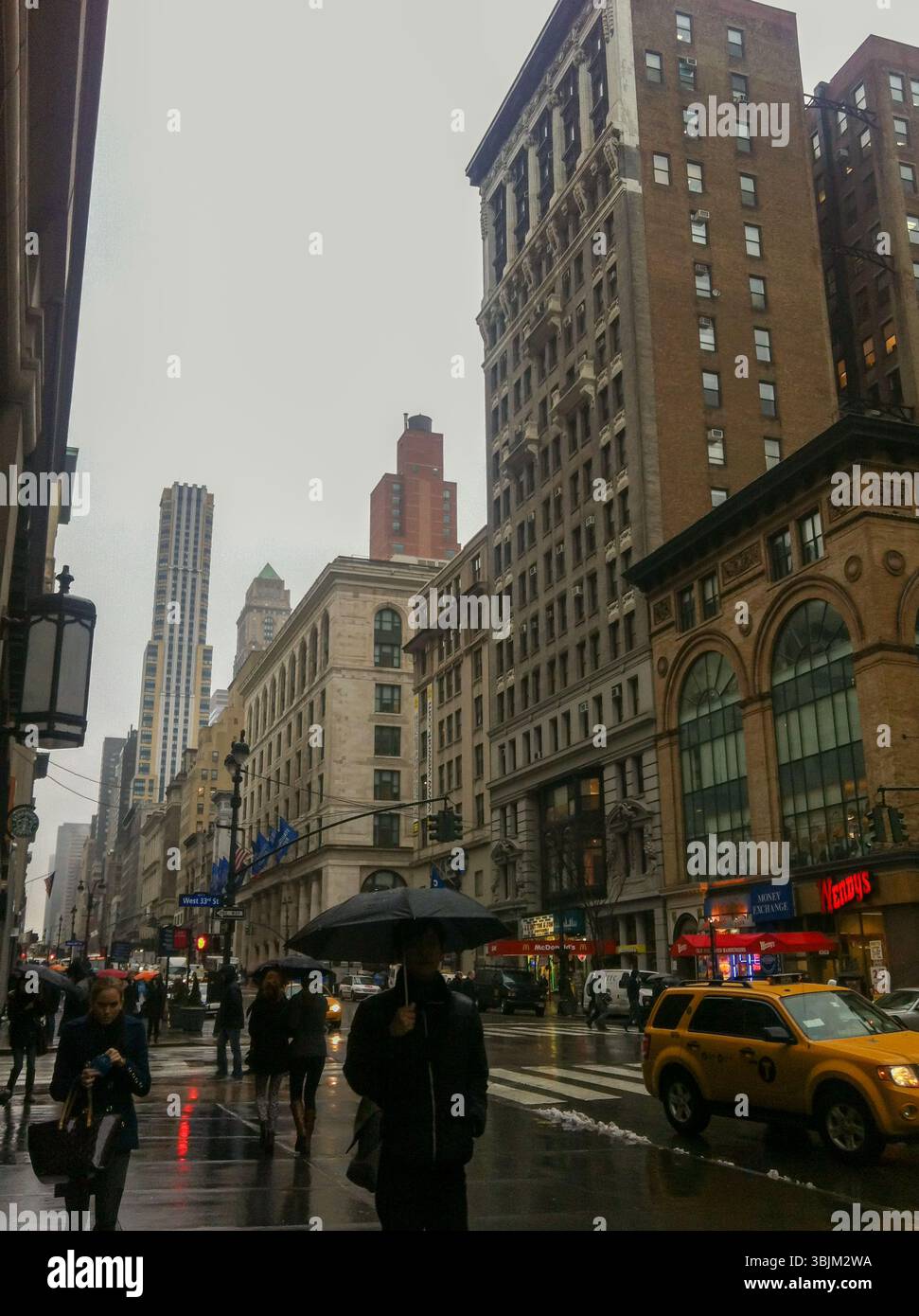NEW YORK, États-Unis – 19 MARS 2013 : des personnes munies de parapluies marchent le long de la Cinquième Avenue sous la pluie. Des taxis jaunes et des devantures de magasins peuvent être vus. Banque D'Images