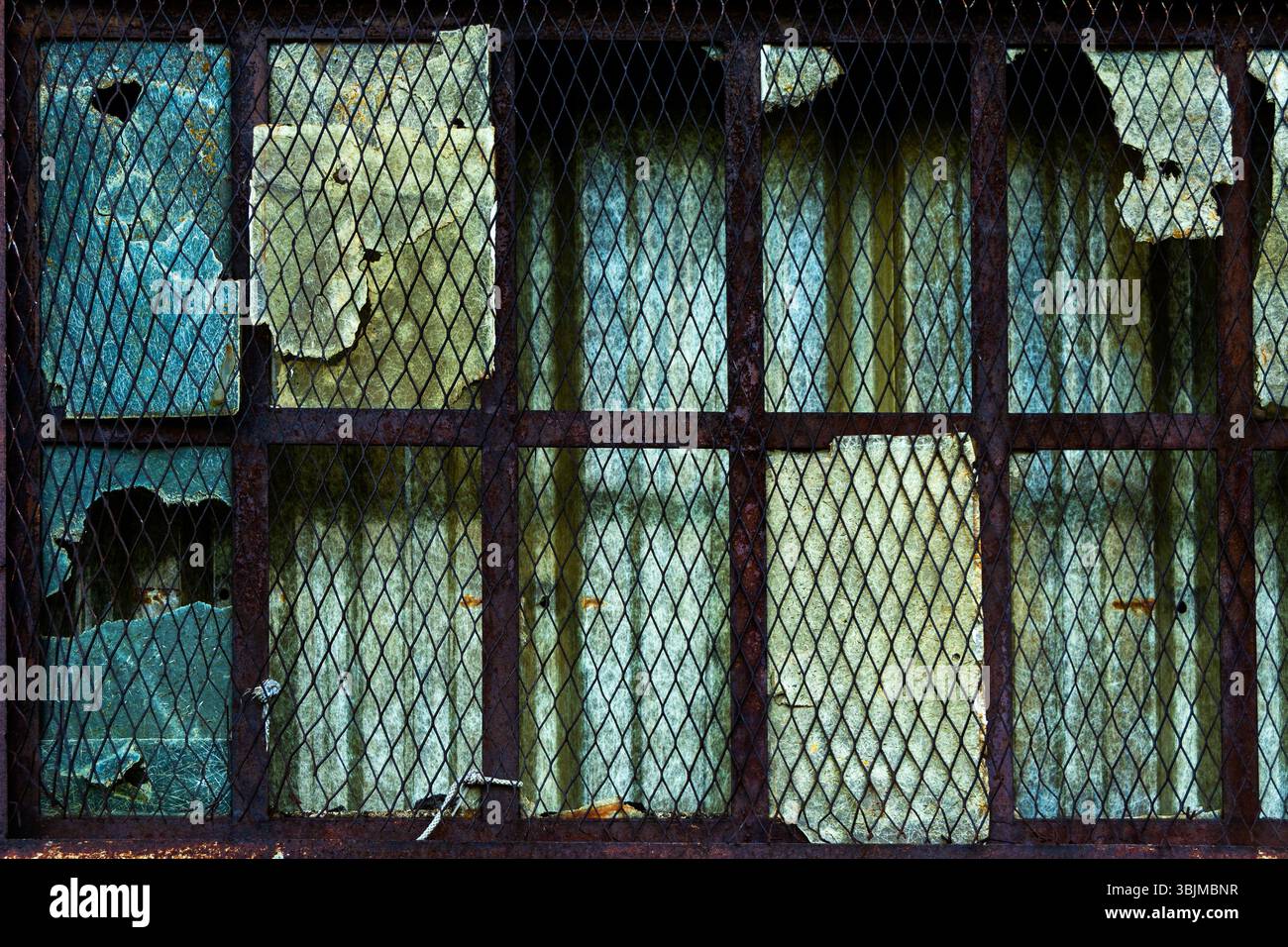 La fenêtre altérée présente du verre endommagé et des barres de métal rouillé, montrant des signes de pourriture et de négligence dans une structure abandonnée. Banque D'Images