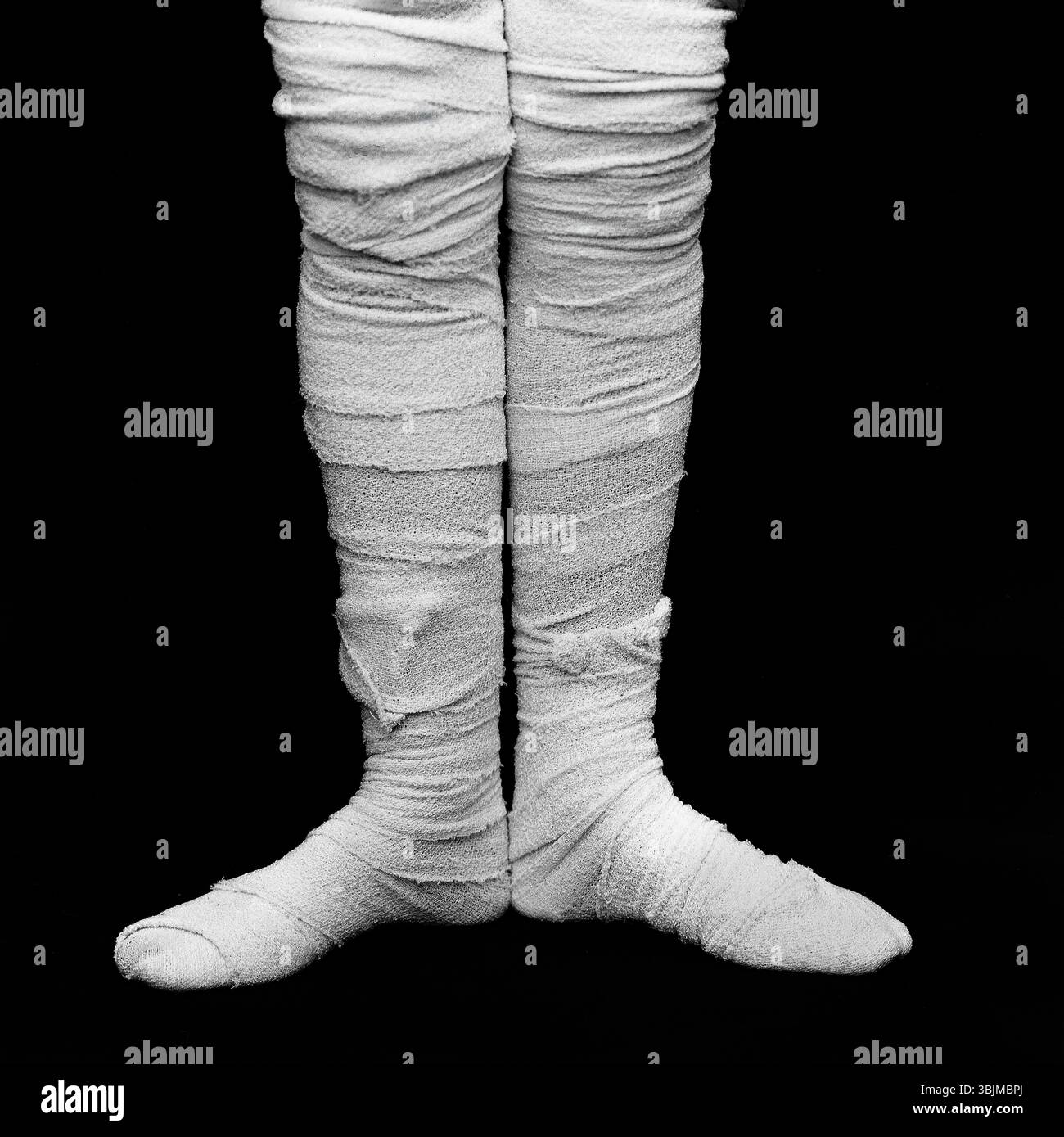 Les jambes bandées sont positionnées étroitement ensemble, mettant en évidence le traitement médical et les soins sur un fond sombre. Banque D'Images