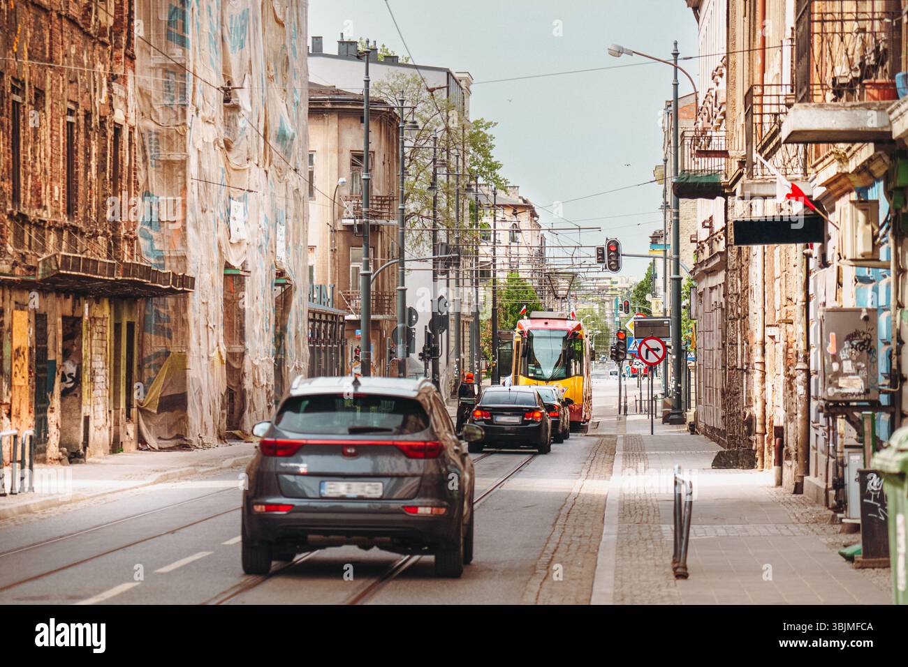 Rue urbaine en cours de rénovation avec des voitures et le tramway dans la ville européenne Lodz Pologne image montre de vieux bâtiments altérés, certains couverts de filet de protection Banque D'Images