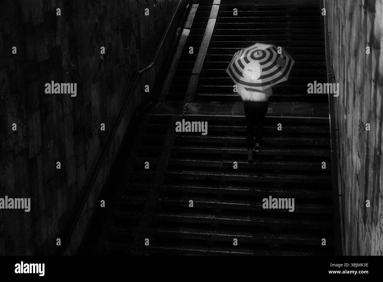Homme sous la pluie marchant avec un parapluie. Personne méconnaissable en flou de mouvement. Banque D'Images