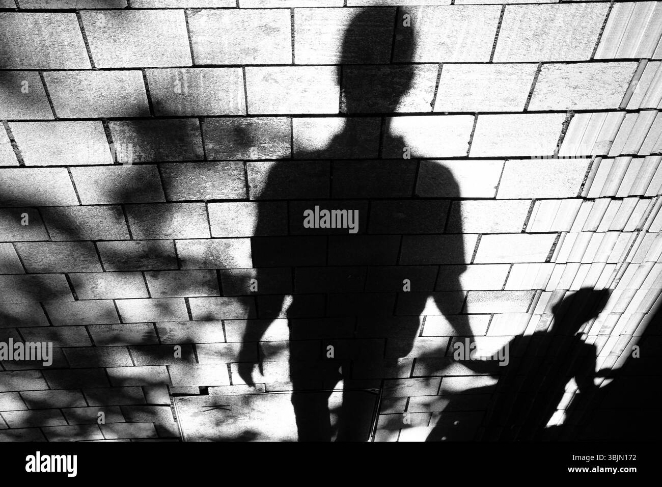 Ombre de silhouette de l'homme marchant main dans la main avec un garçon sur le trottoir de la rue de la ville en noir et blanc contraste élevé Banque D'Images