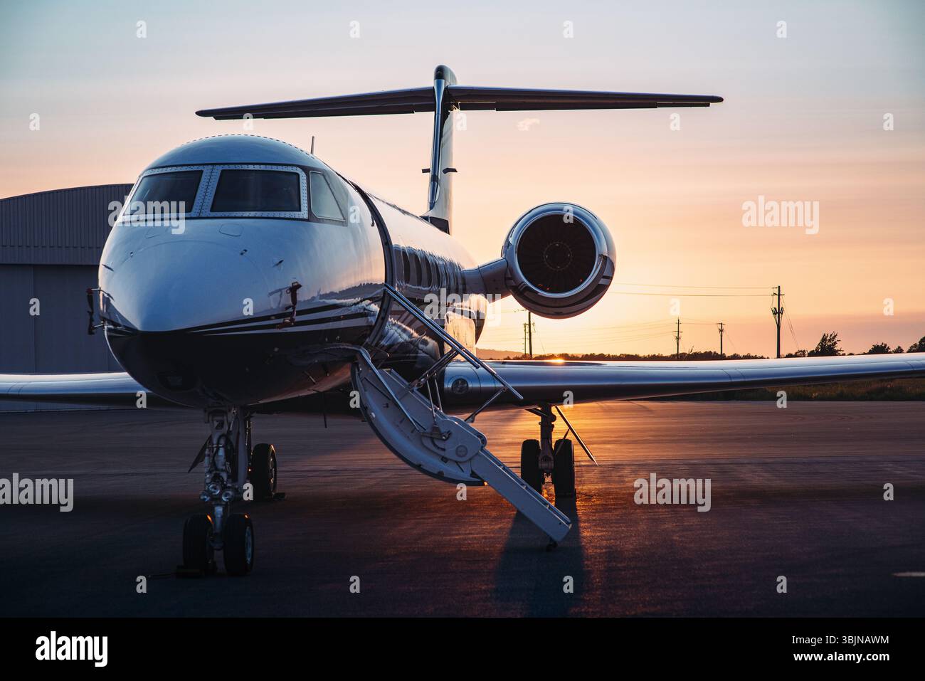 Jet privé élégant sur tarmac au coucher du soleil avec escaliers d'embarquement, hangar à proximité, baigné de lumière dorée chaude. Banque D'Images