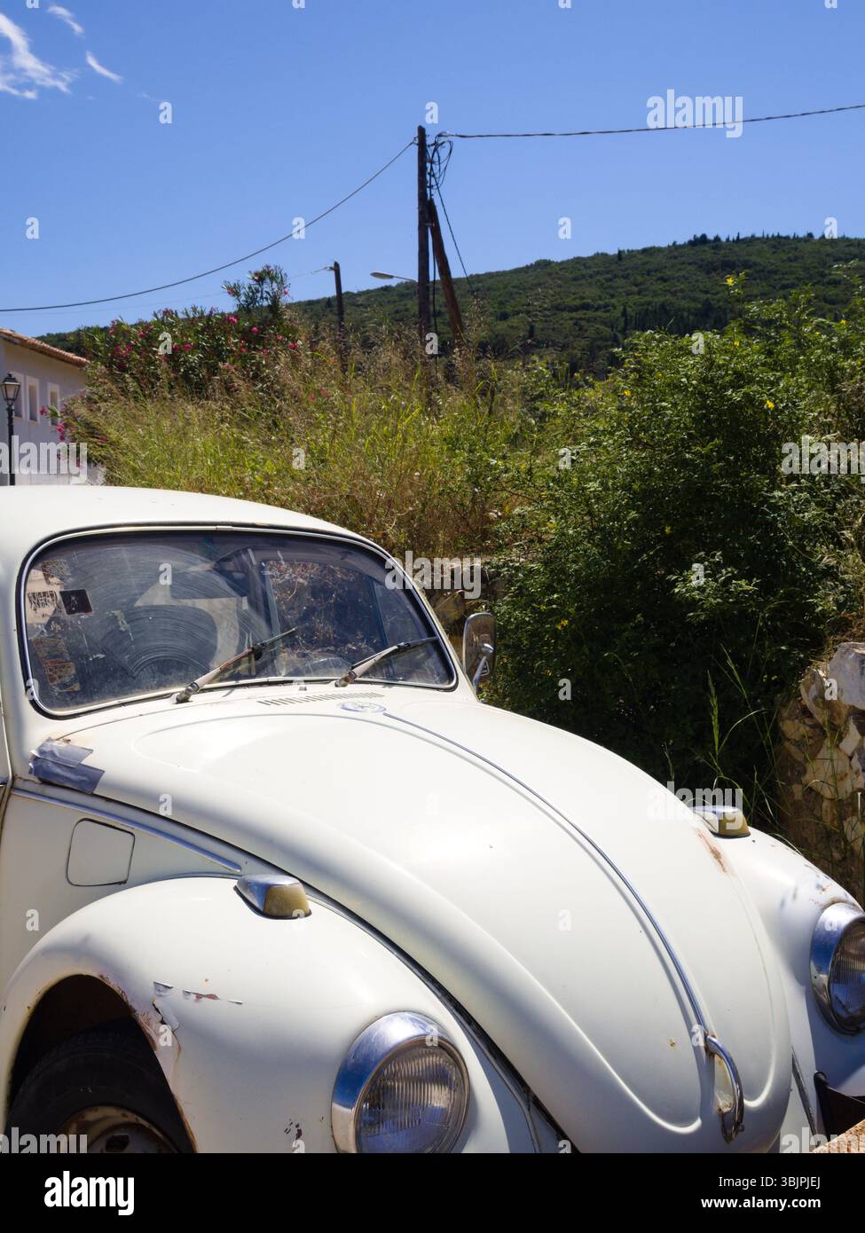 Partie d'une voiture blanche rétro dans une scène de campagne ensoleillée, entourée d'herbe de prairie et de paysage broussailleux sous le ciel sans nuages. Banque D'Images