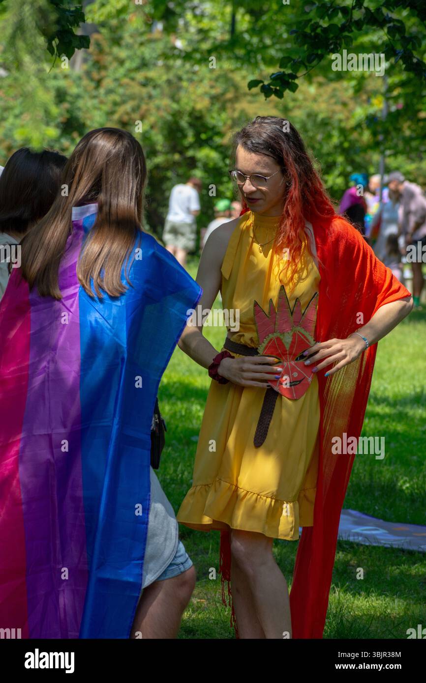 Deux participants drapés dans des drapeaux arc-en-ciel et bisexuels discutent dans le parc Łazienki, Varsovie, dans la voïvodie de Masovian, en Pologne, lors du défilé de la fierté en juin 2025 Banque D'Images