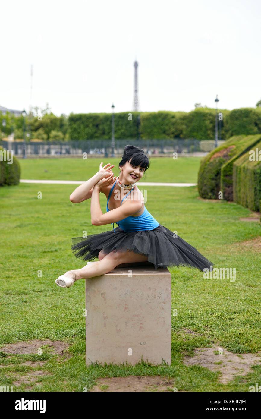 Ballerine assise sur piédestal en tutu noir souriant à l'extérieur Banque D'Images