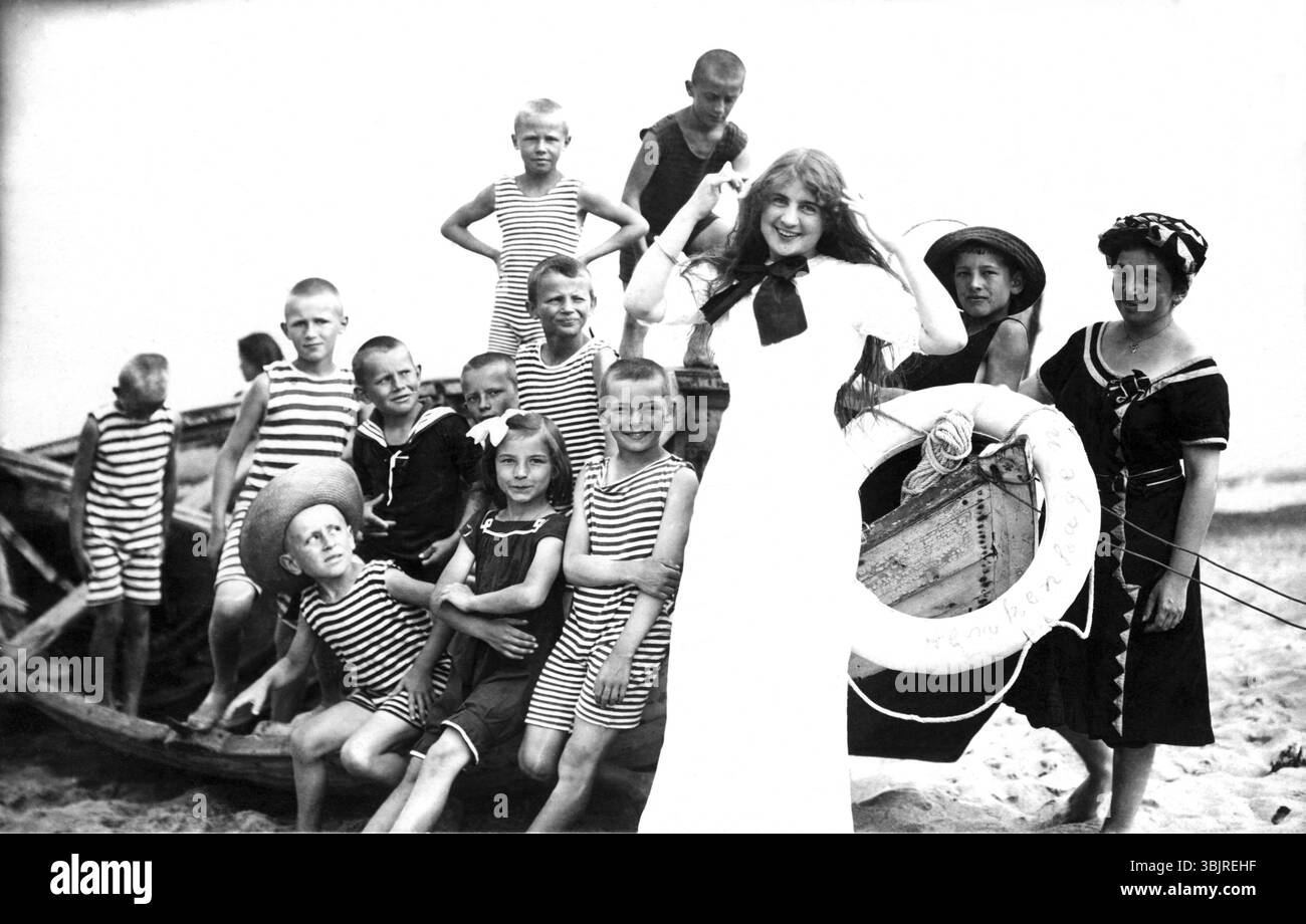 Temps libre des enfants, années 1920, enfants en vêtements rayés et une femme posant souriant sur la plage à côté d'un vieux bateau, photo historique Banque D'Images