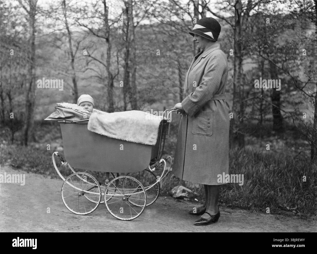 Femme poussant la poussette, années 1920, femme avec un chapeau debout à côté d'une poussette et riant avec le bébé couché dedans, photo historique Banque D'Images