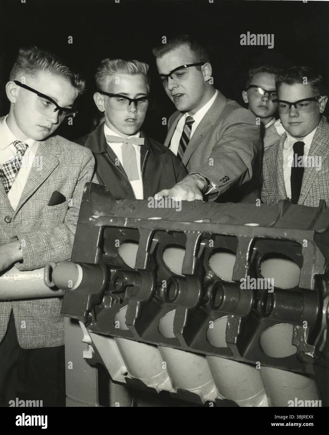 L'élève semble s'ennuyer tandis que l'enseignant explique, 1950s, groupe d'hommes examinant un modèle technique. Tous portant des costumes et regardant avec intérêt l'objet, Banque D'Images