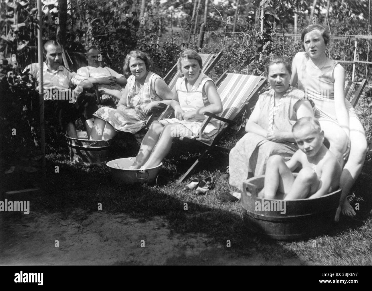 Été chaud dans le jardin, années 1930, les gens assis dans un jardin et se rafraîchissant dans des récipients remplis d'eau, photo historique Banque D'Images