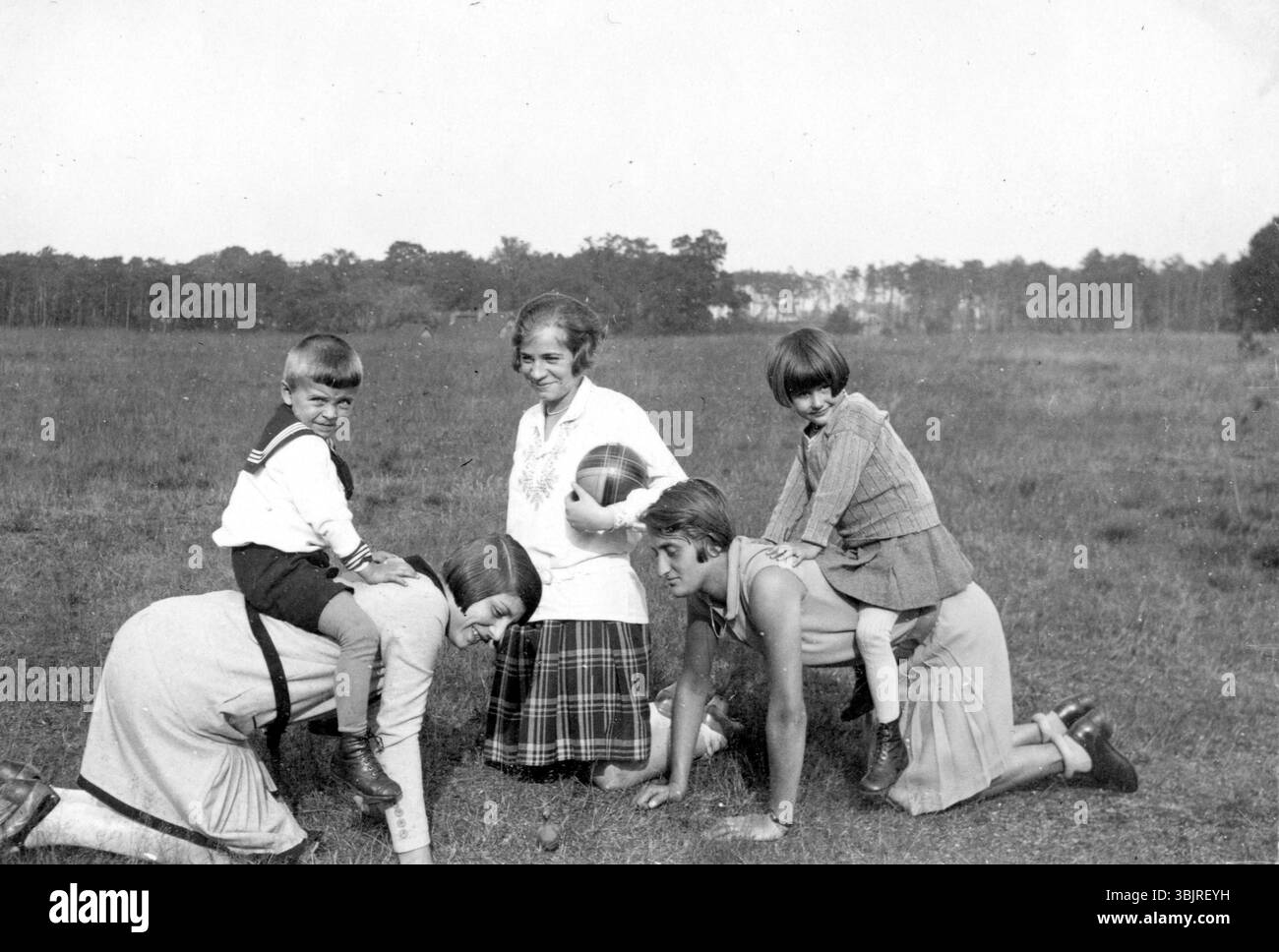 Deux enfants chevauchant sur le dos de leur mère, années 1930, des enfants jouant dans le pré avec deux adultes dans une ambiance joyeuse, photo historique Banque D'Images