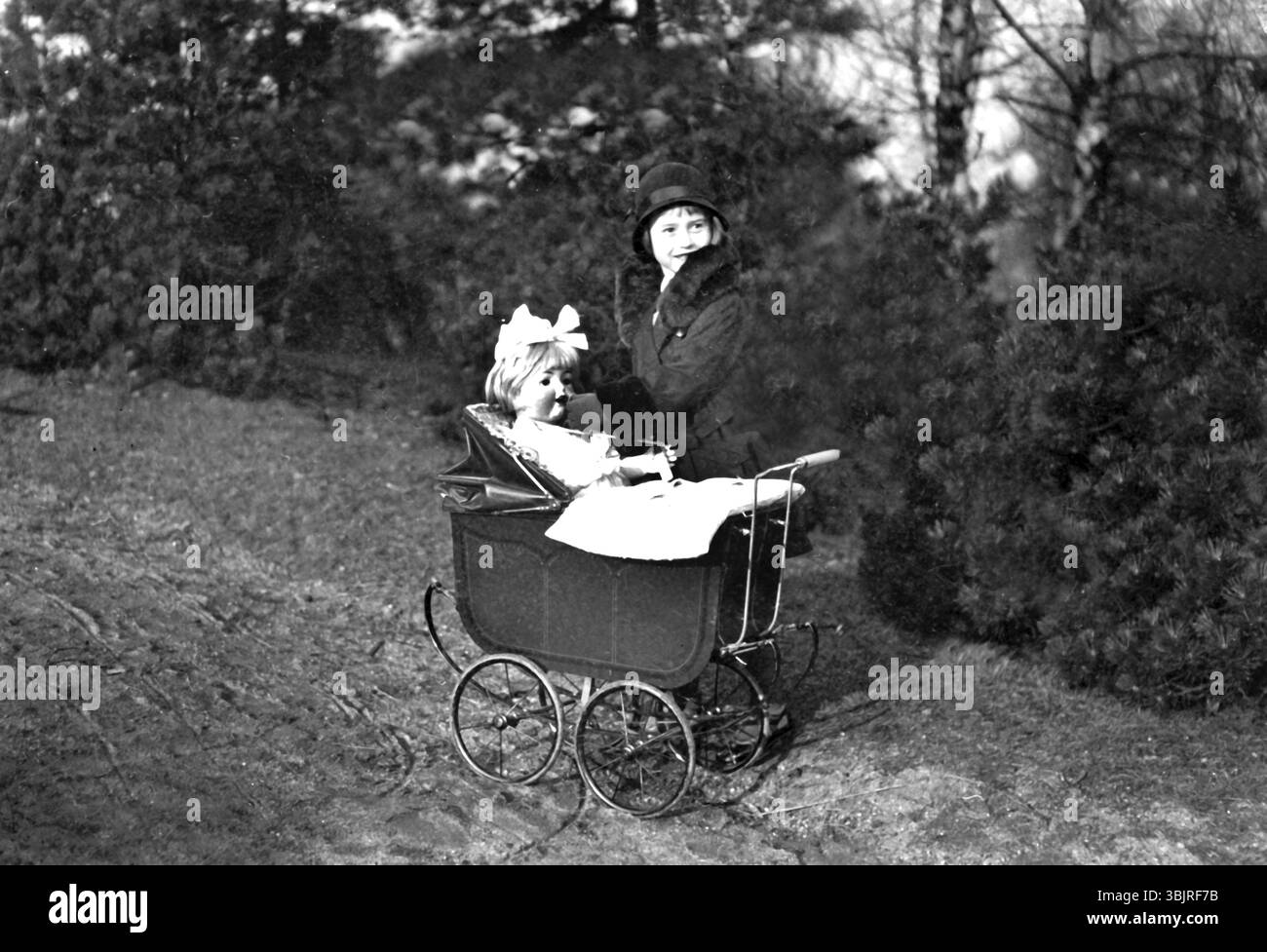 Fille jouant avec une poupée, années 1920, femme avec chapeau et collier de fourrure poussant une poussette antique dans la forêt, photo historique Banque D'Images