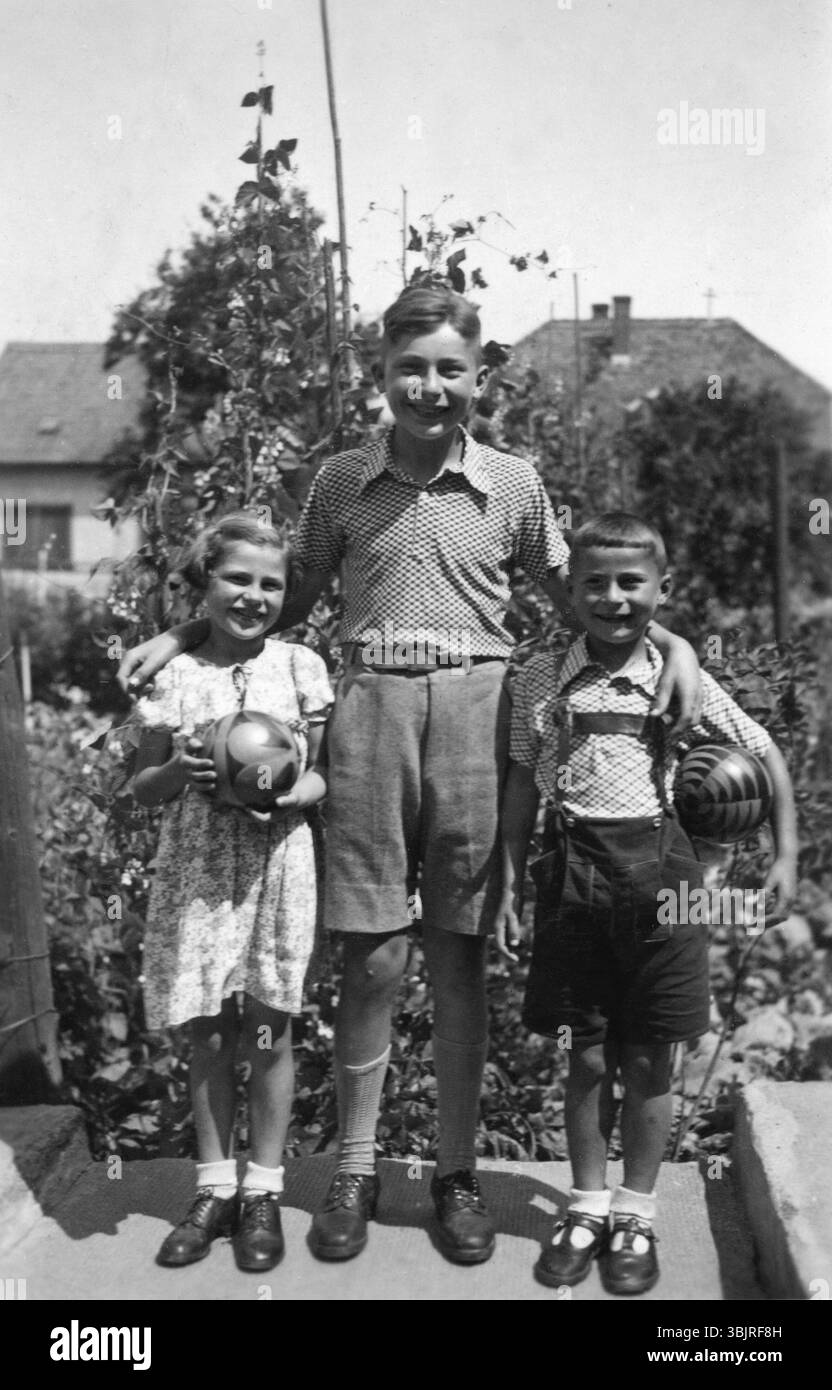 Frères et sœurs avec grand frère, 1950 ans, trois enfants posant avec des balles dans un jardin et souriant à la caméra, photo historique Banque D'Images