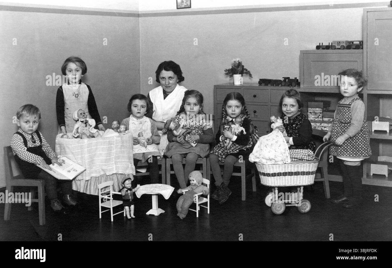 Jouets de groupe de maternelle, années 1930, enfants avec femme dans la chambre, jouer avec des poupées et des jouets à une petite table, photo historique Banque D'Images