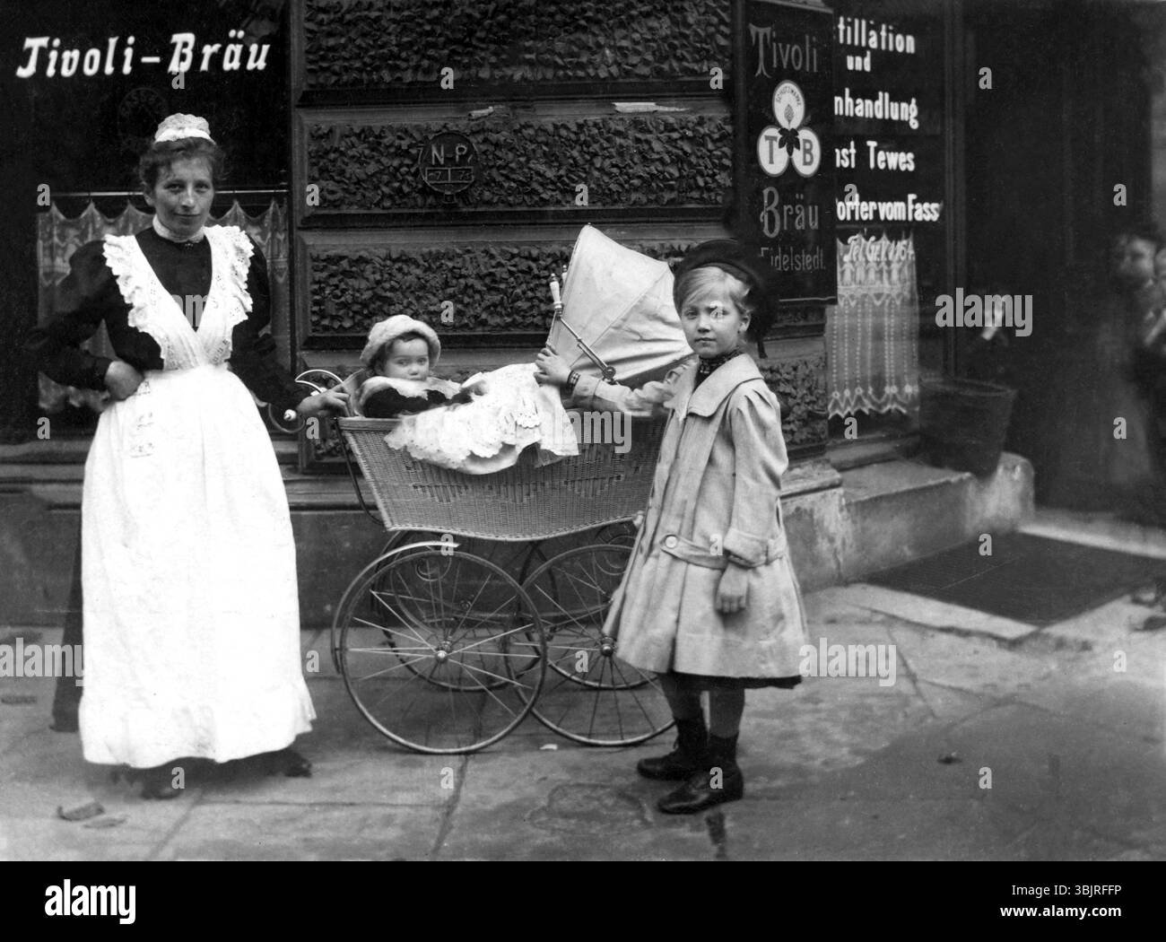 Nounou avec enfants, vers 1910, Une femme avec deux enfants devant un bâtiment historique avec des panneaux publicitaires, photo historique Banque D'Images
