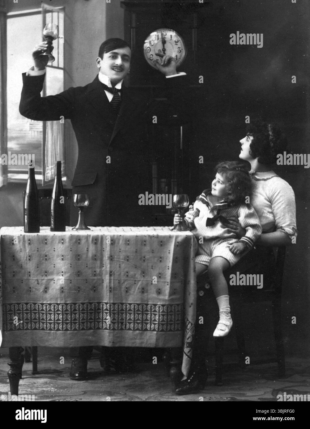 Nouvel an, homme levant le verre tandis que femme avec enfant assis à table, photographie à l'ancienne, photographie historique Banque D'Images