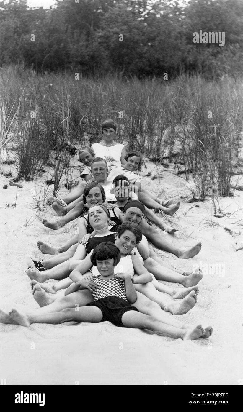 Groupe sur la plage, années 1930, enfants en maillots de bain noir et blanc souriant sur le sable et profitant de la journée d'été, photo historique Banque D'Images