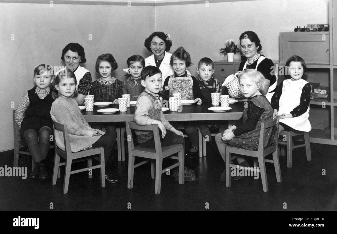Groupe de maternelle, années 1930, scène maternelle avec enfants assis, femme à la table avec des tasses, humeur joyeuse, photo historique Banque D'Images