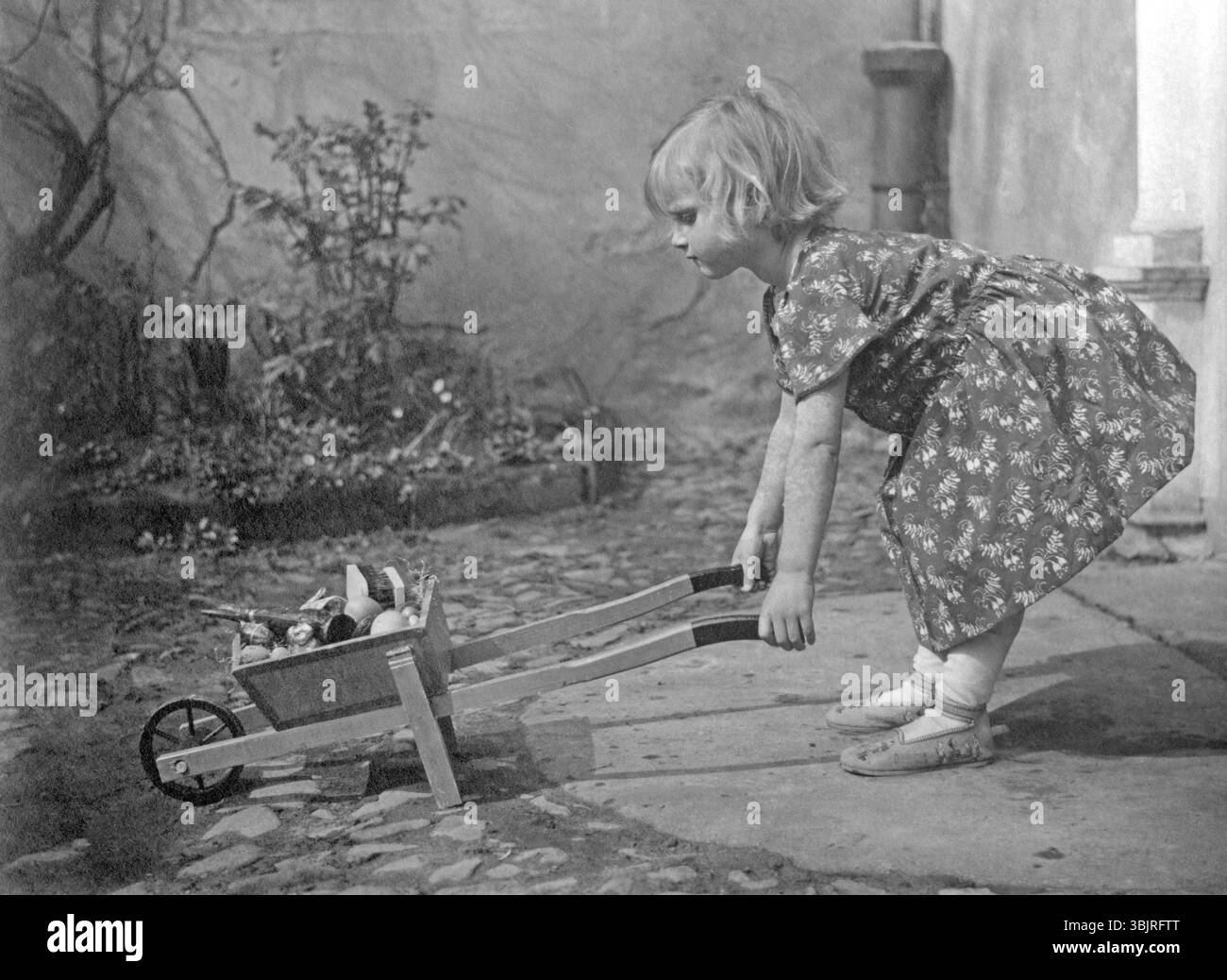 Fille avec brouette, années 1920, Une fille jouant dans le jardin avec une brouette, photo historique Banque D'Images