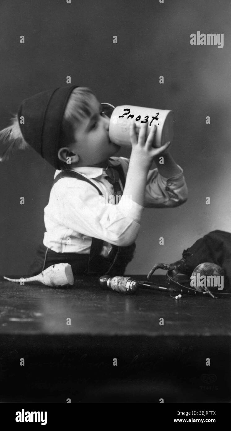 Enfant avec une tasse de bière, années 1930, Un garçon avec un chapeau boit d'une tasse de bière avec « Cheers » écrit dessus, photo historique Banque D'Images