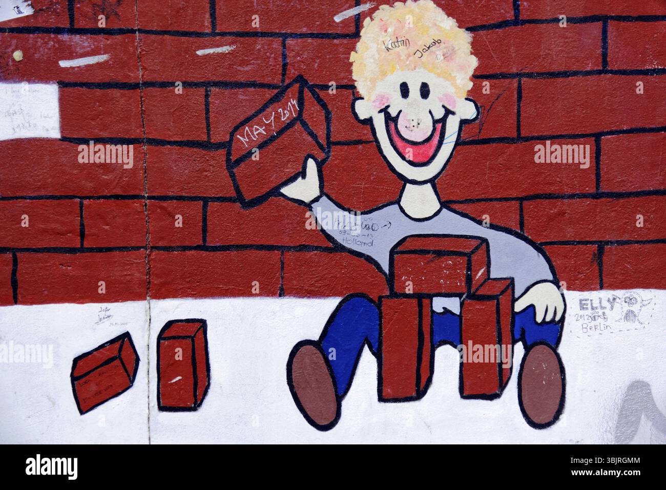 Image joyeuse de style dessin animé d'un enfant jouant avec des briques devant un mur de briques, Graffiti sur le mur de Berlin à la East Side Gallery, Berlin, GE Banque D'Images