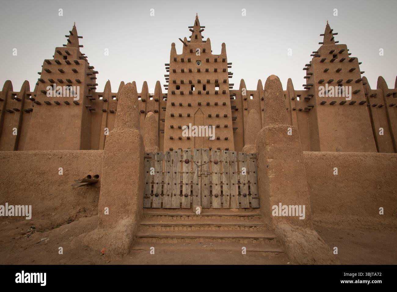La façade de la Grande Mosquée de Djenné au Mali à l'aube, montrant sa façade emblématique en briques de boue, sa porte centrale et ses trois imposants minarets. Banque D'Images