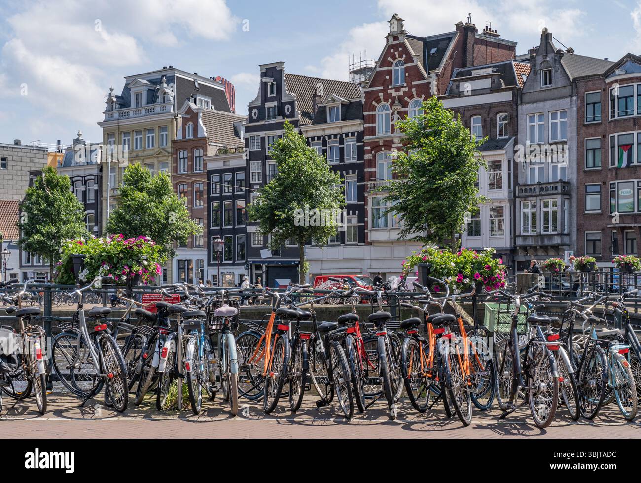 Amsterdam, pays-Bas - 7 juin 2024 : vélos garés sur le pont avec des maisons et des magasins en arrière-plan Banque D'Images