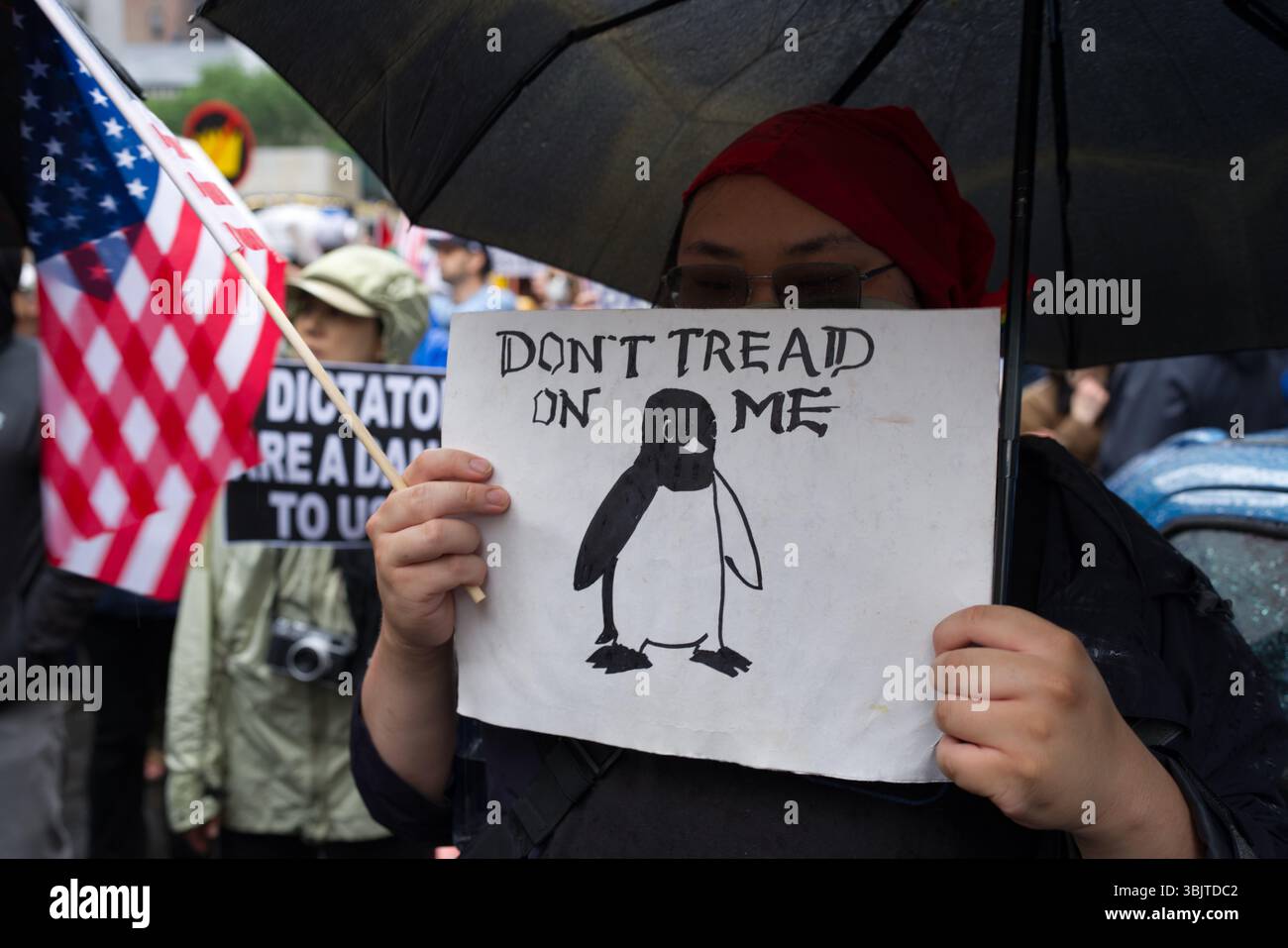 Une personne à une manifestation tient une pancarte qui dit "ne me tapisse pas" avec un dessin d'un pingouin. Ils portent un foulard et des lunettes rouges, et tiennent une ombre Banque D'Images