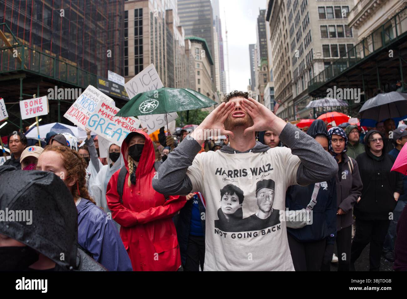 Un homme portant un t-shirt « Harris Walz - Not Got Back » crie lors d'une manifestation dans une rue de la ville. La pluie tombe, et d'autres manifestants tiennent des pancartes avec divers Banque D'Images