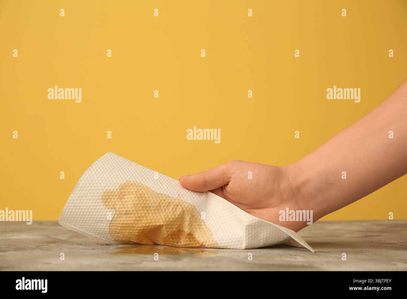 Femme essuyant le café renversé avec une serviette en papier sur la table grunge grunge près du mur jaune Banque D'Images