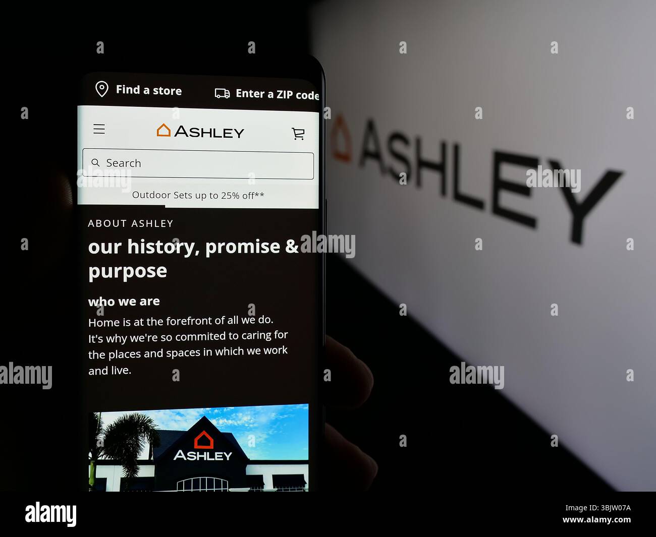 Stuttgart, Allemagne - 2025 : personne tenant un téléphone portable avec la page web de la société américaine Ashley Furniture Industries Inc sur l'écran devant le logo. Banque D'Images